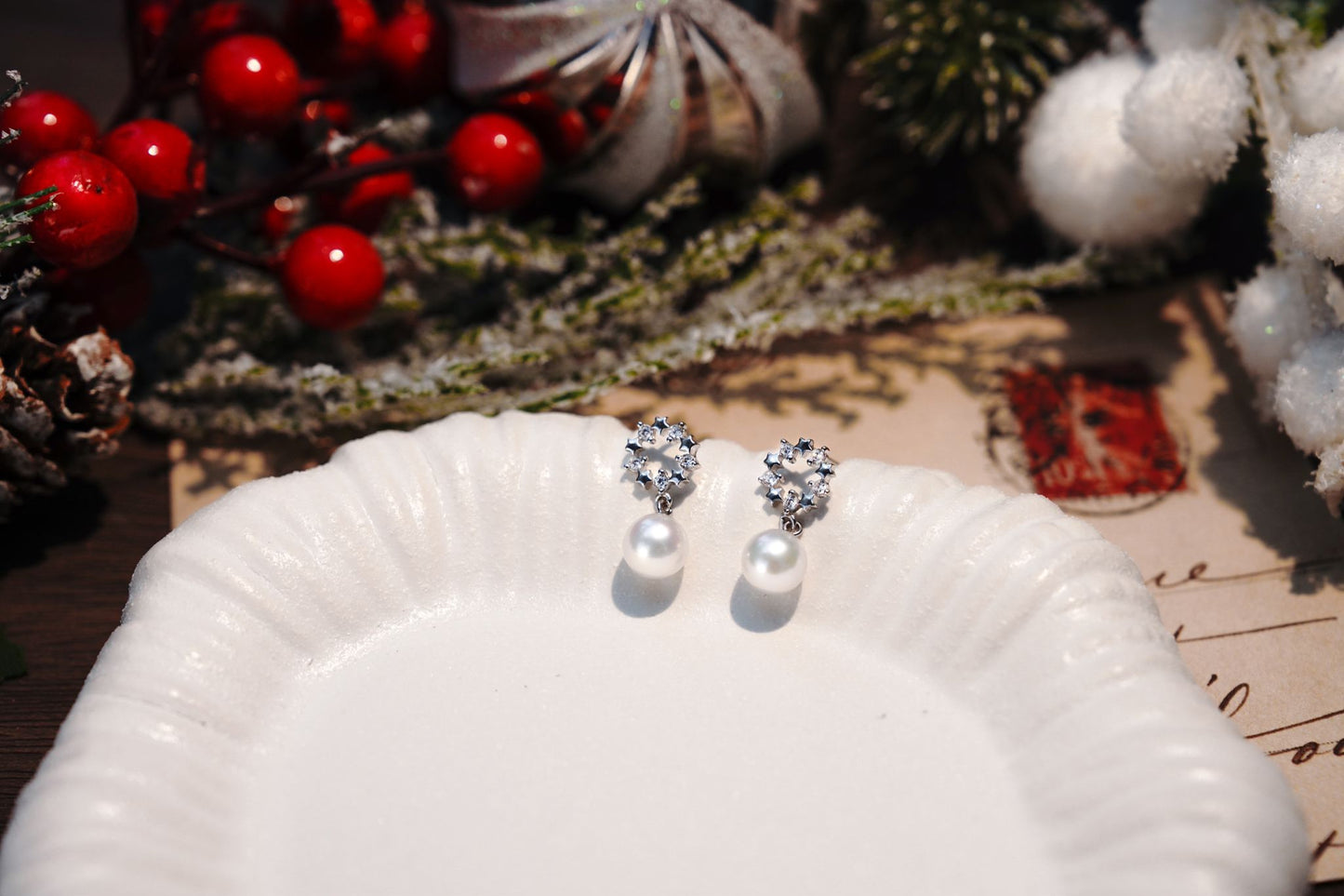 Cyrene's sparkling wreath and pearl drop earrings resting on a white shell plate, a perfect elegant jewelry gift
