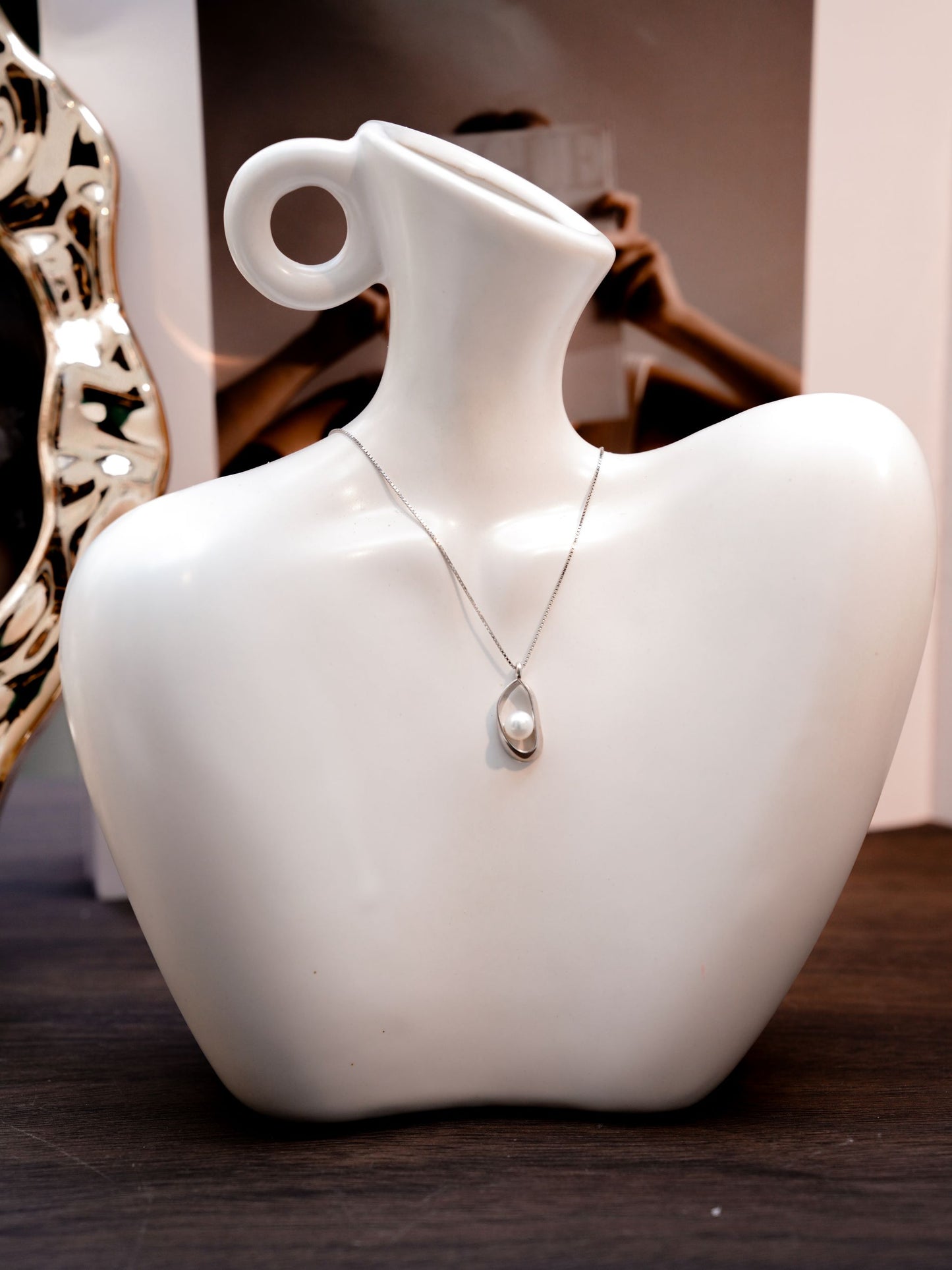 A geometric silver necklace by Cyrene with a dainty pearl inside an open frame, offering a clean and modern aesthetic.