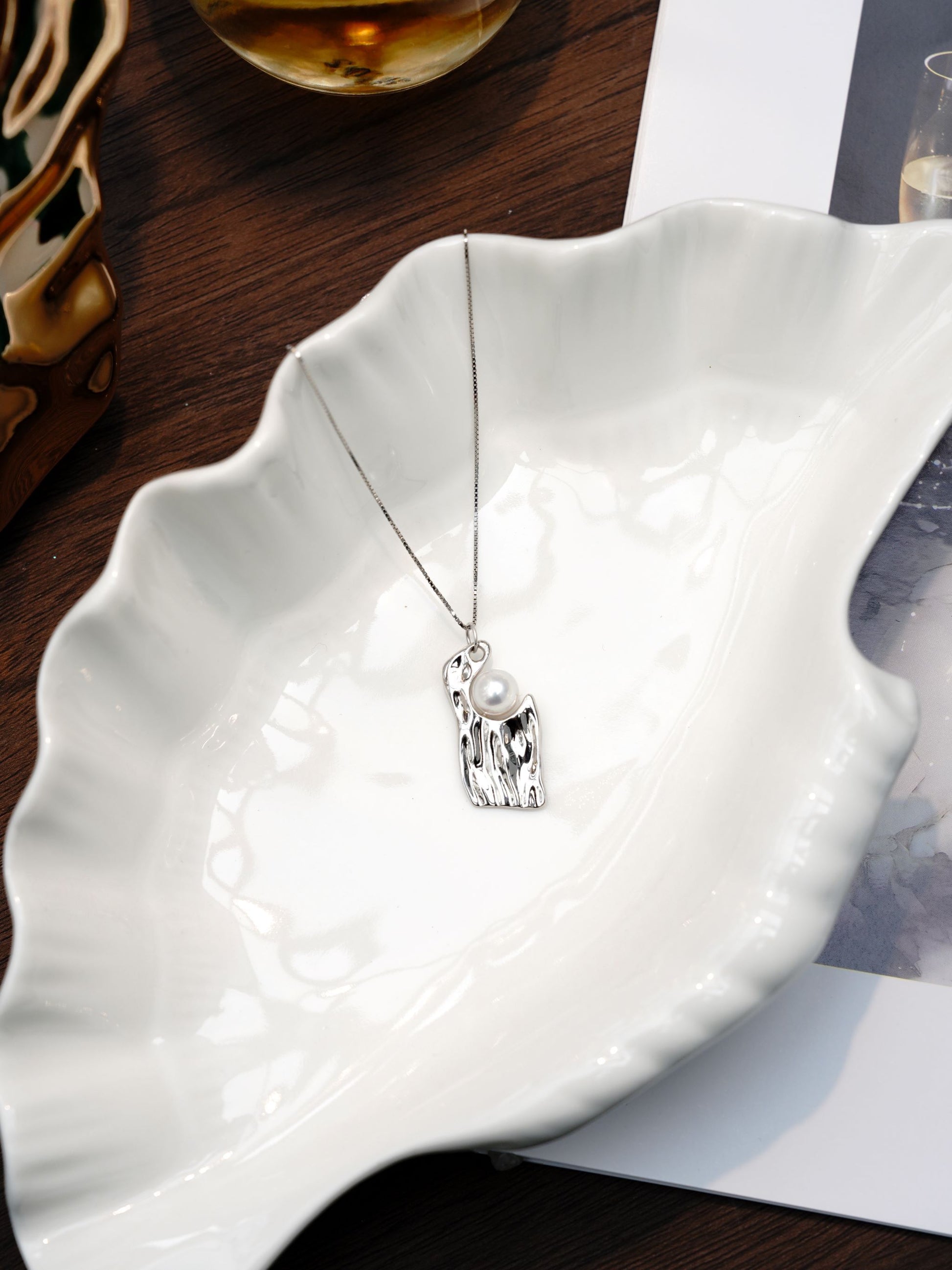 Contemporary sculpted silver jewelry design showcasing Cyrene's irregular pearl necklace resting elegantly on a white ceramic dish.