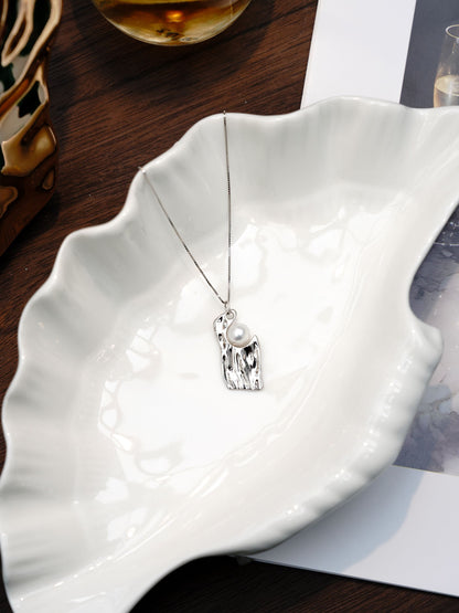 Contemporary sculpted silver jewelry design showcasing Cyrene's irregular pearl necklace resting elegantly on a white ceramic dish.