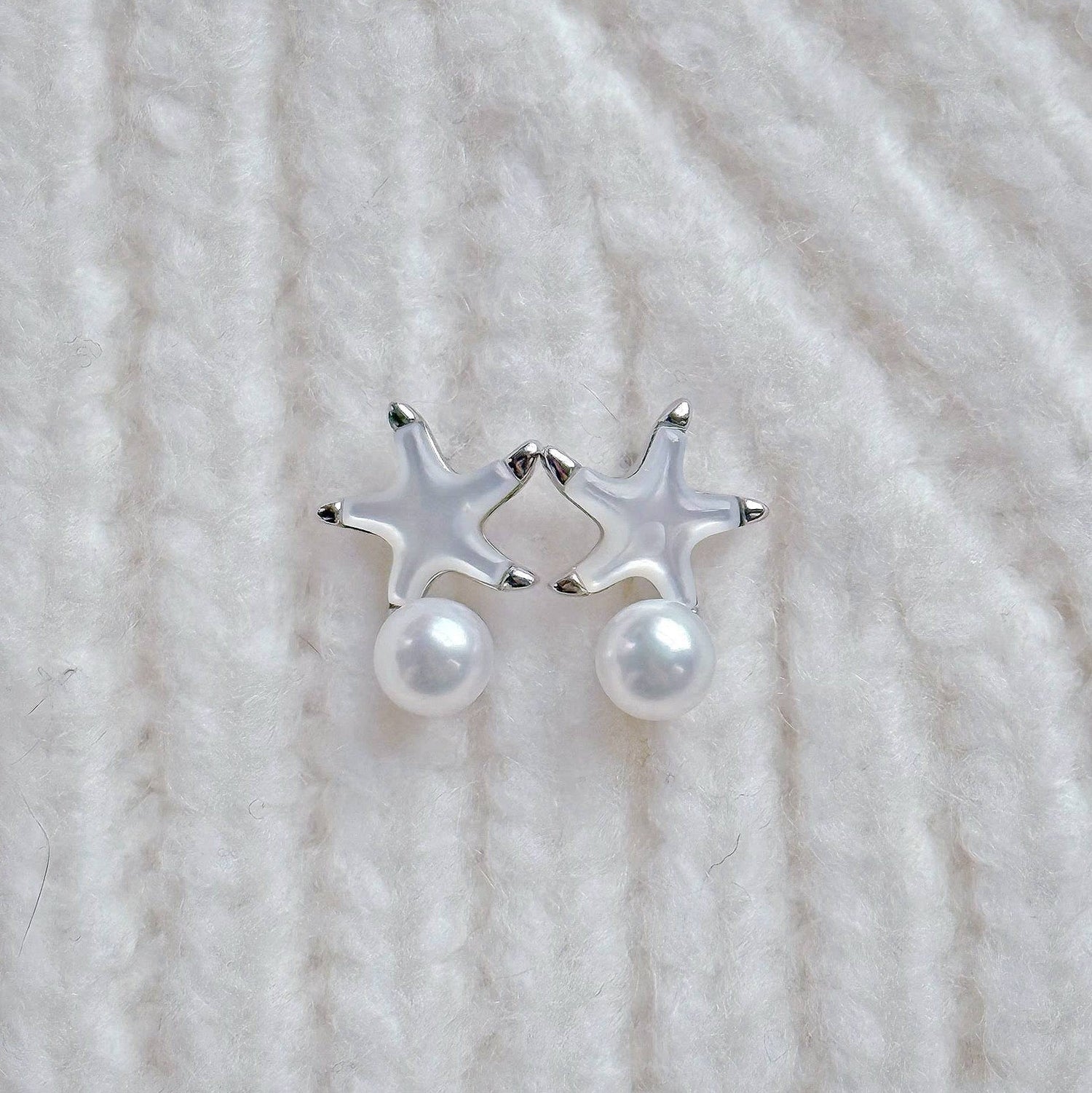 Close-up of Cyrene's delicate mother-of-pearl starfish earrings with elegant silver edging and a high-luster freshwater pearl drop