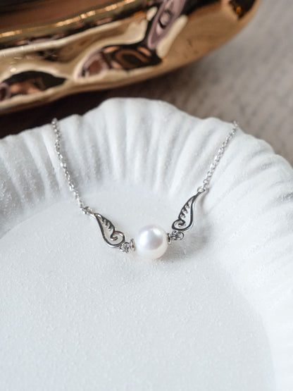 Close-up of a dainty Cyrene silver bracelet featuring delicate angel wings and a beautiful freshwater pearl.