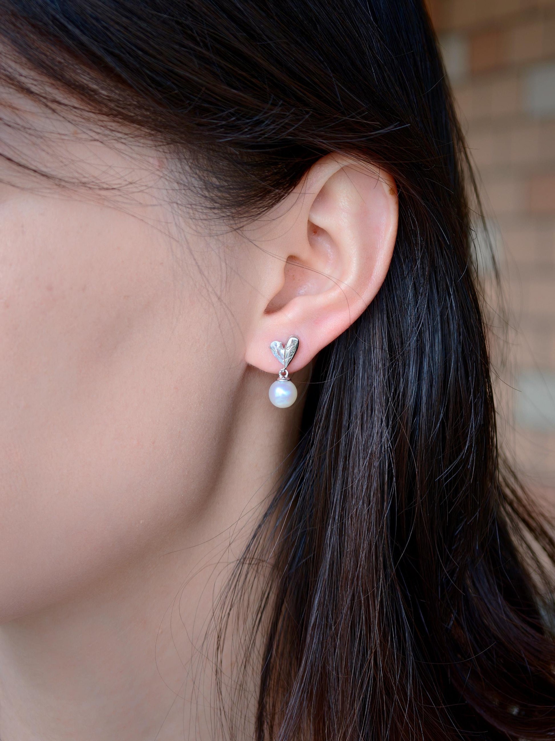 Cyrene by Elsie Demi Pearl Earrings worn in natural light showing 7-8mm round pearl and silver heart detail
