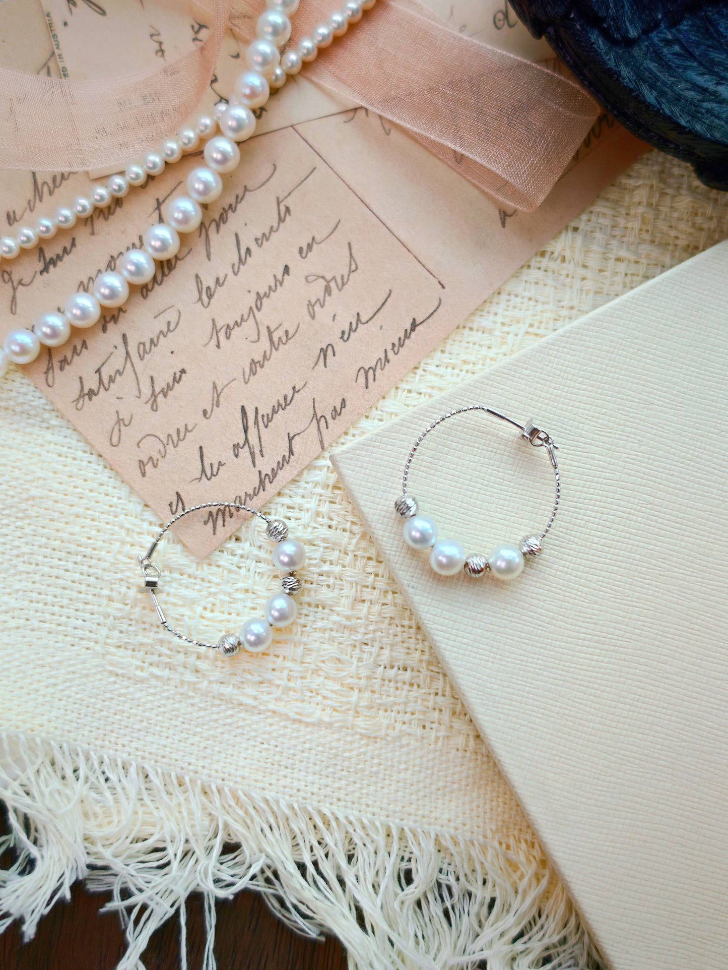 Cyrene Halo Pearl Hoop Earring pair flat lay, aurora freshwater pearl and silver hoop on vintage letter background