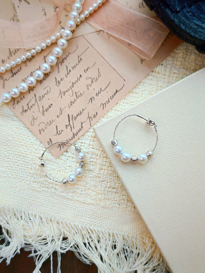 Cyrene Halo Pearl Hoop Earring pair flat lay, aurora freshwater pearl and silver hoop on vintage letter background