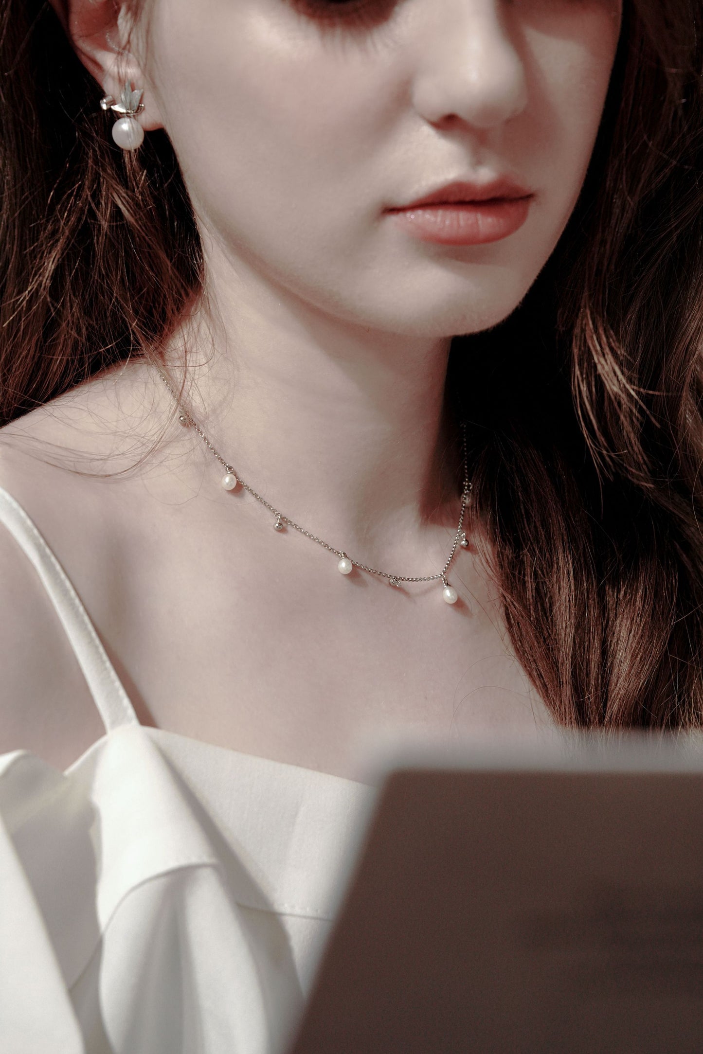 A versatile effortless chic look featuring a woman reading, styled with Cyrene's dynamic silver chain necklace with delicate pearl drops