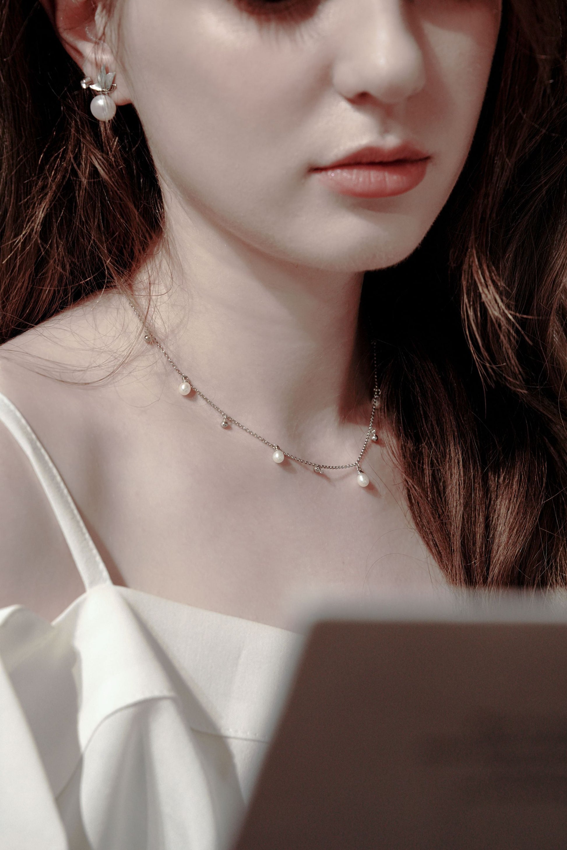 A versatile effortless chic look featuring a woman reading, styled with Cyrene's dynamic silver chain necklace with delicate pearl drops