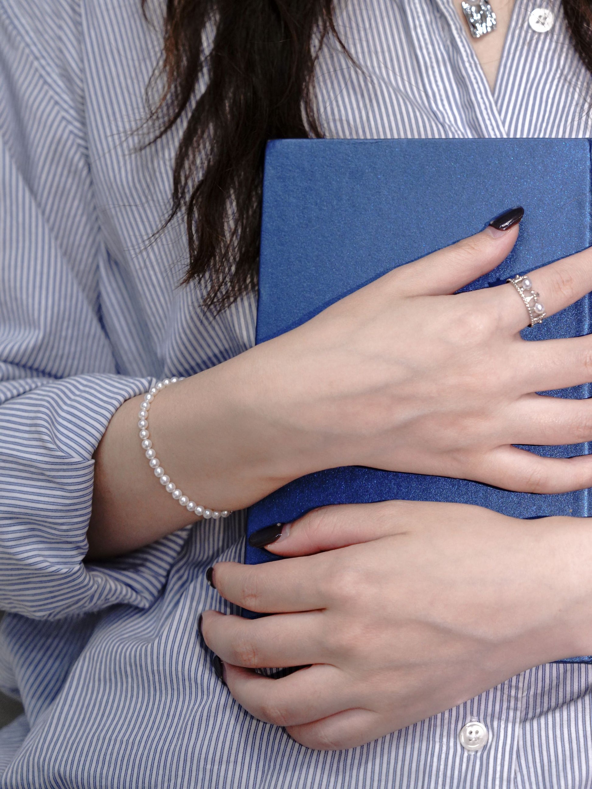 Light academia aesthetic featuring a woman holding a book, highlighting the clean and gentle full strand pearl bracelet by Cyrene.