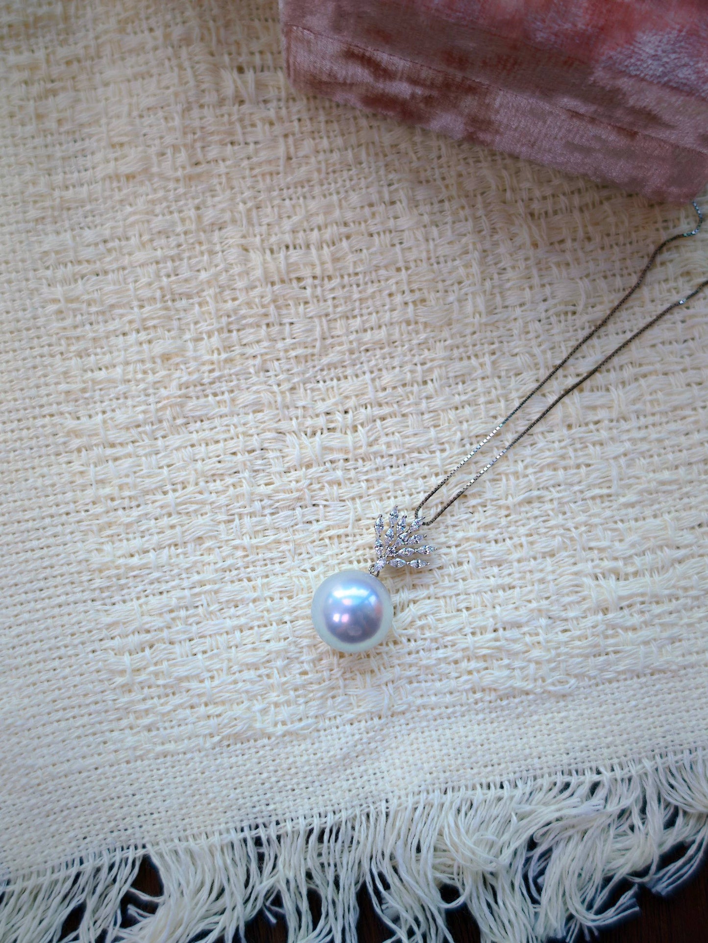 Cyrene Lone Drop Pearl Pendant flatlay on textured fabric — South Sea pearl pendant with CZ leaf detail