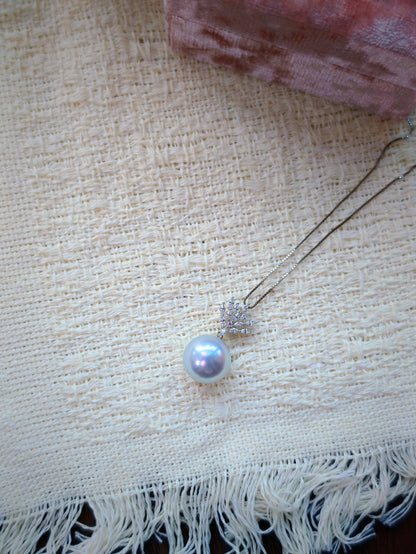 Cyrene Lone Drop Pearl Pendant flatlay on textured fabric — South Sea pearl pendant with CZ leaf detail