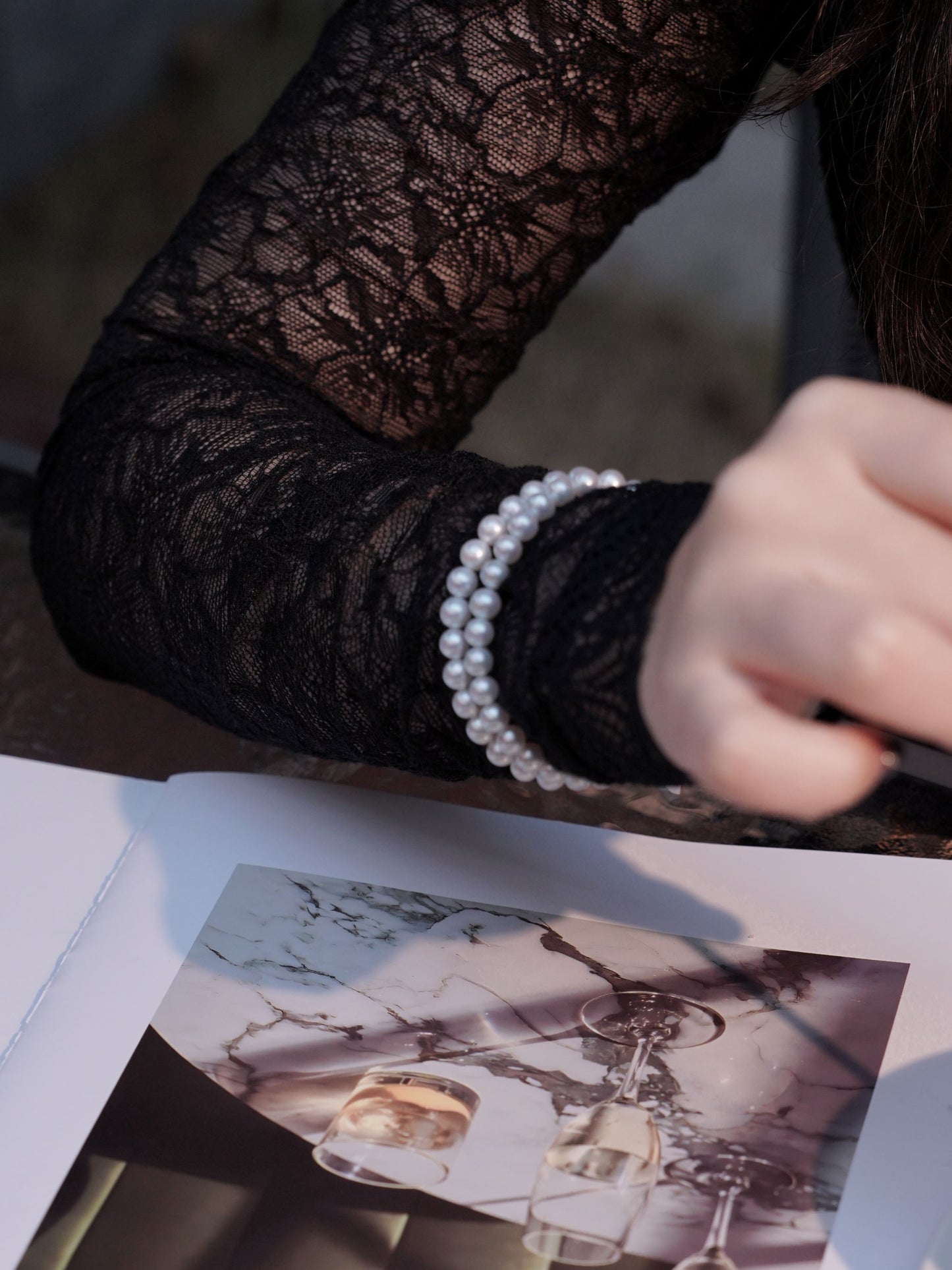 Model wearing a luxurious double-strand pearl bracelet from Cyrene over a black lace sleeve, highlighting its radiant luster.