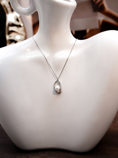 Close-up of a minimalist irregular silver frame pendant featuring a delicate freshwater pearl by Cyrene