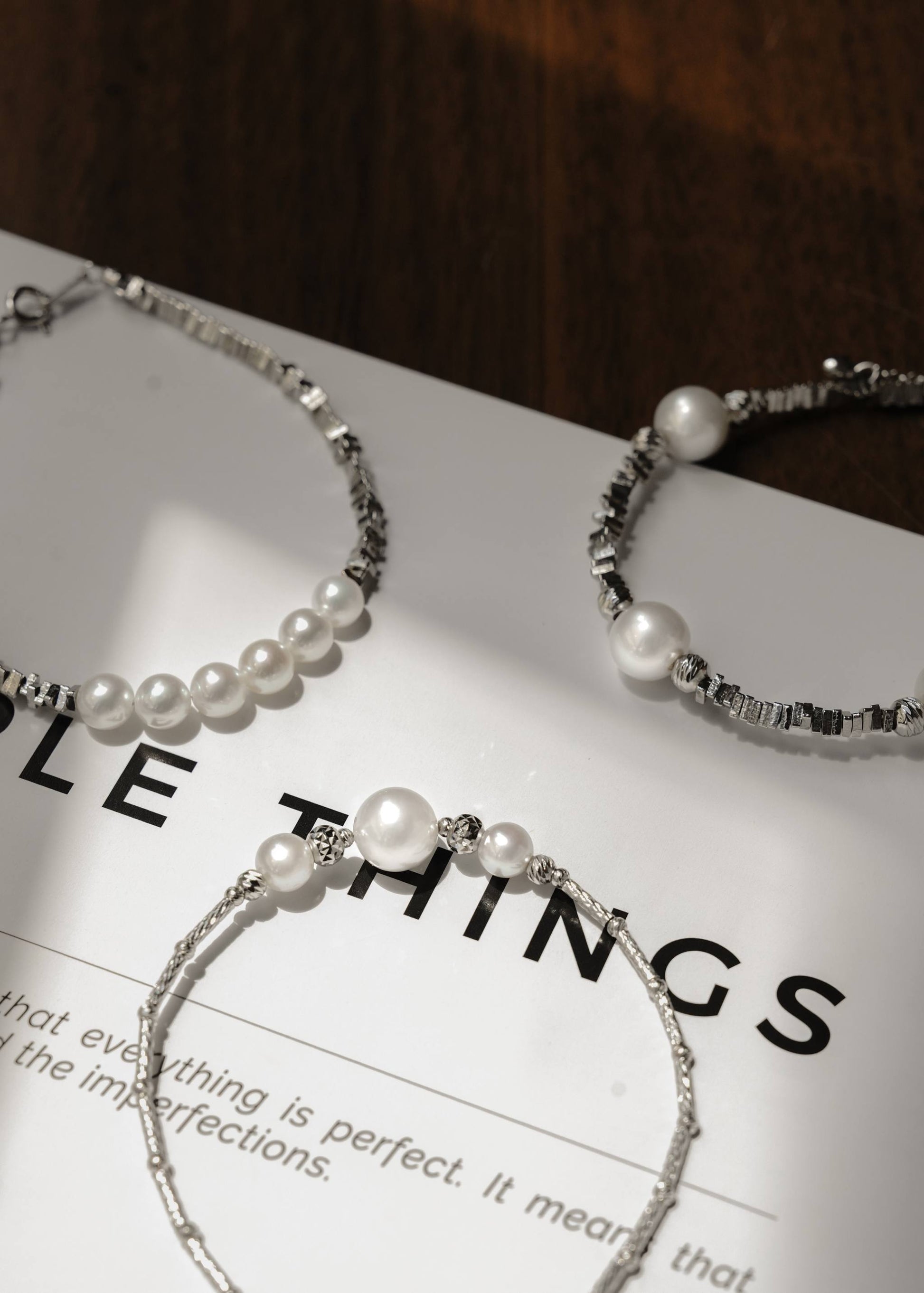 Minimalist Cyrene jewelry highlighting a stunning three-pearl centerpiece and carved silver tube chain, displayed on a modern magazine