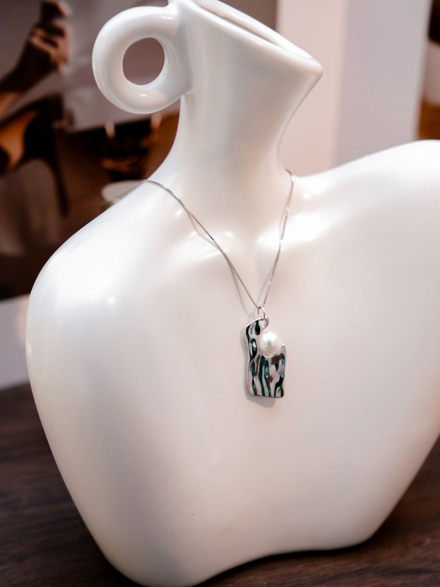 A modern molten silver plate pendant by Cyrene, capturing dynamic light reflections around a classic freshwater pearl.