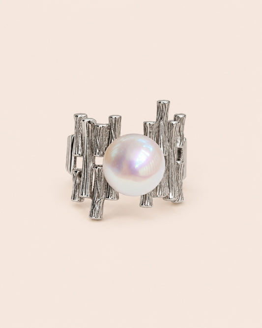 A silver-toned textured ring featuring a central white pearl, photographed on a clean, solid cream-colored background.
