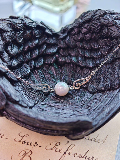 Close-up of Cyrene Pinion Pearl Bracelet, silver wing charms flanking single freshwater pearl on ultra-fine chain