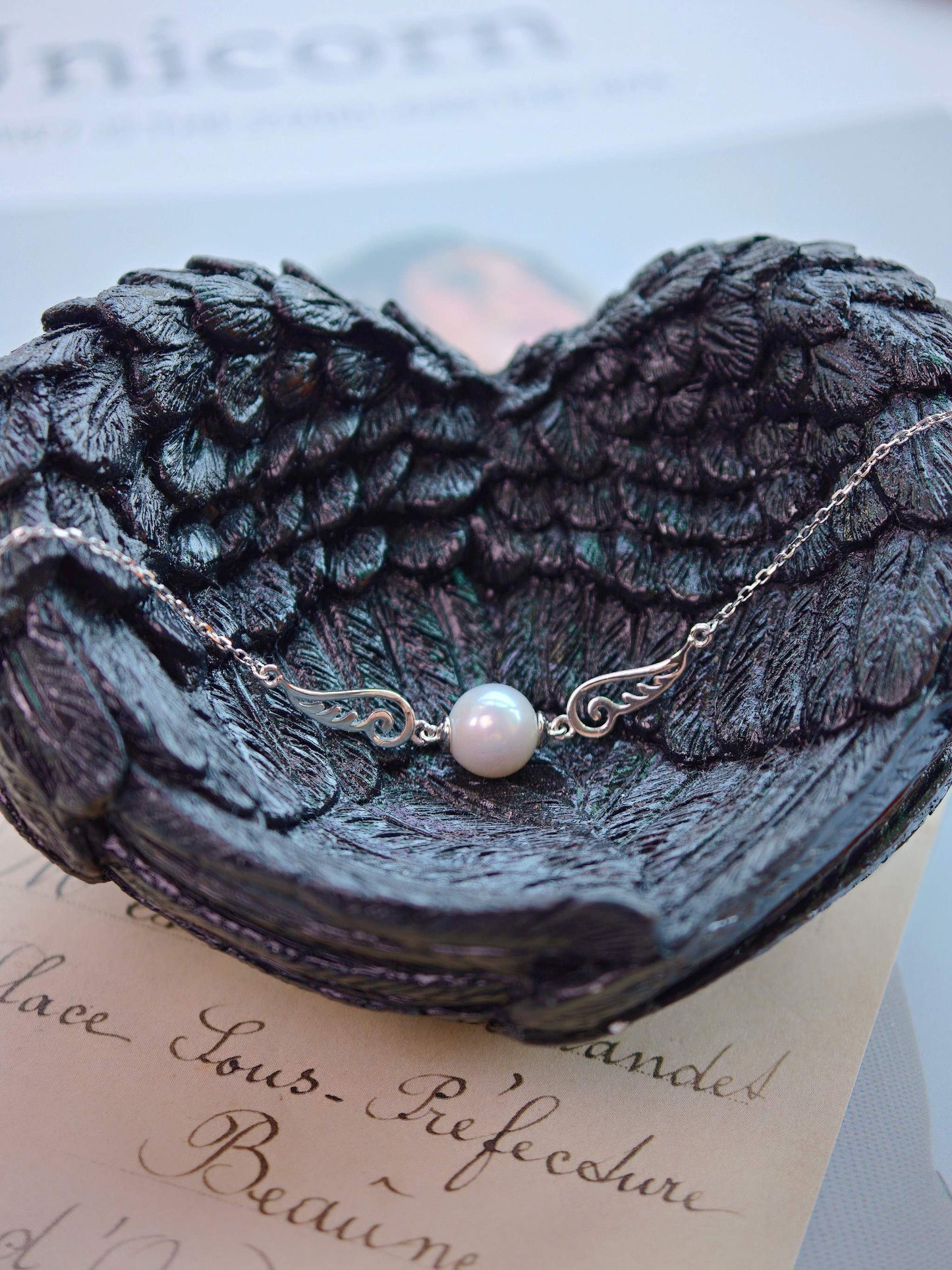 Cyrene Pinion Pearl Bracelet flat lay on dark angel wing base, 925 silver wing detail with freshwater pearl center