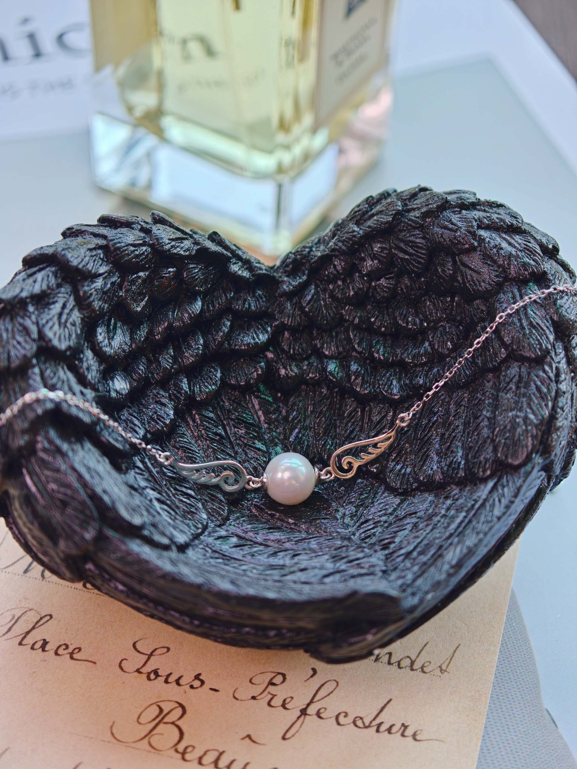 Cyrene Pinion Pearl Bracelet on dark wing base with perfume background, sterling silver and freshwater pearl bracelet