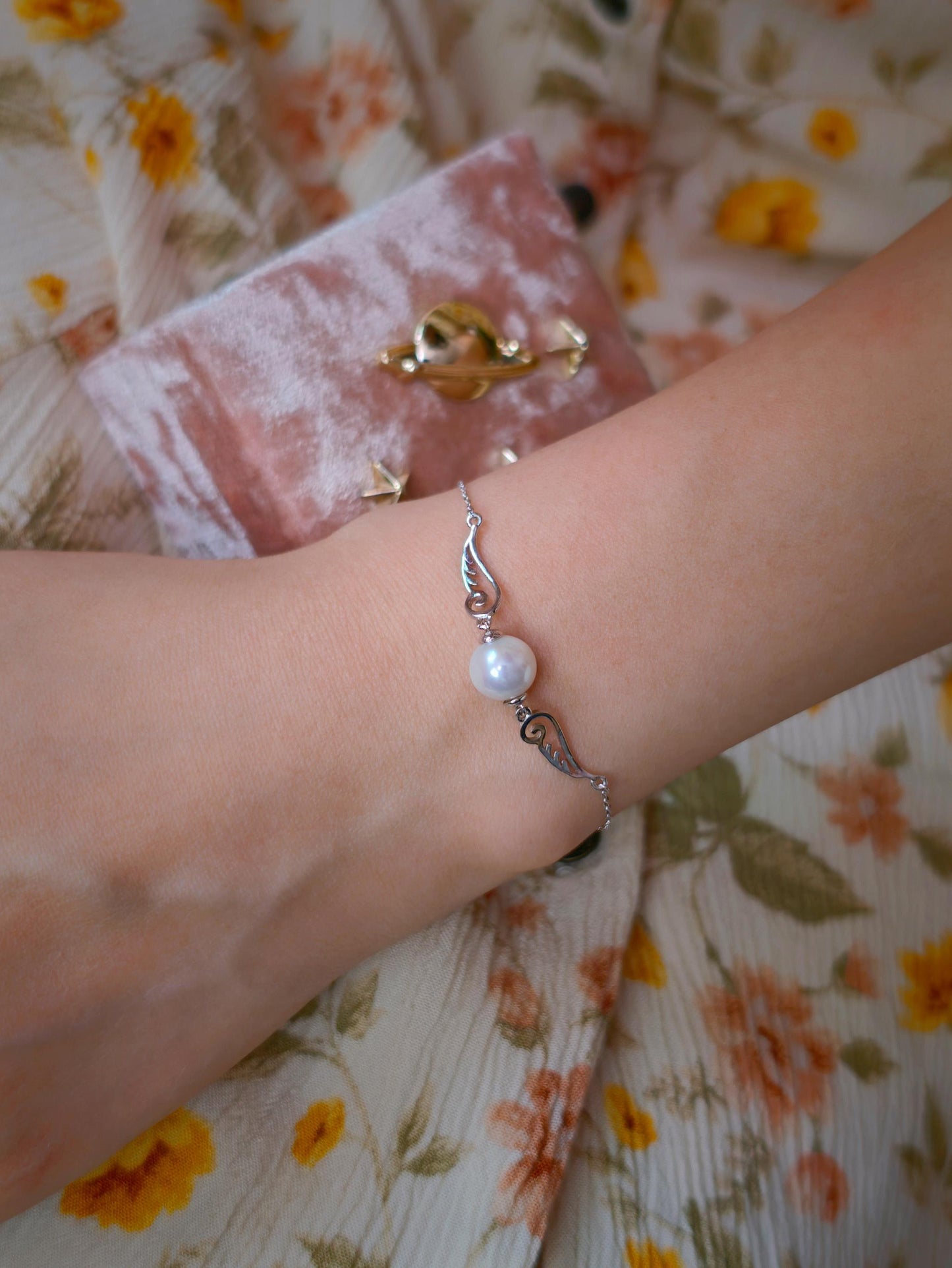 Model wearing Cyrene Pinion Pearl Bracelet on wrist, delicate silver wing bracelet with pearl, adjustable chain