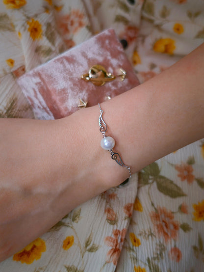 Model wearing Cyrene Pinion Pearl Bracelet on wrist, delicate silver wing bracelet with pearl, adjustable chain