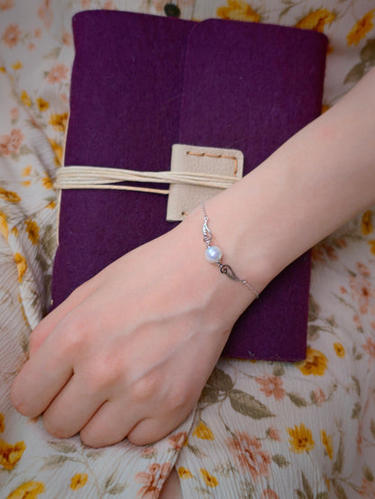 Cyrene Pinion Pearl Bracelet on model wrist with purple journal, freshwater pearl and 925 silver wing bracelet