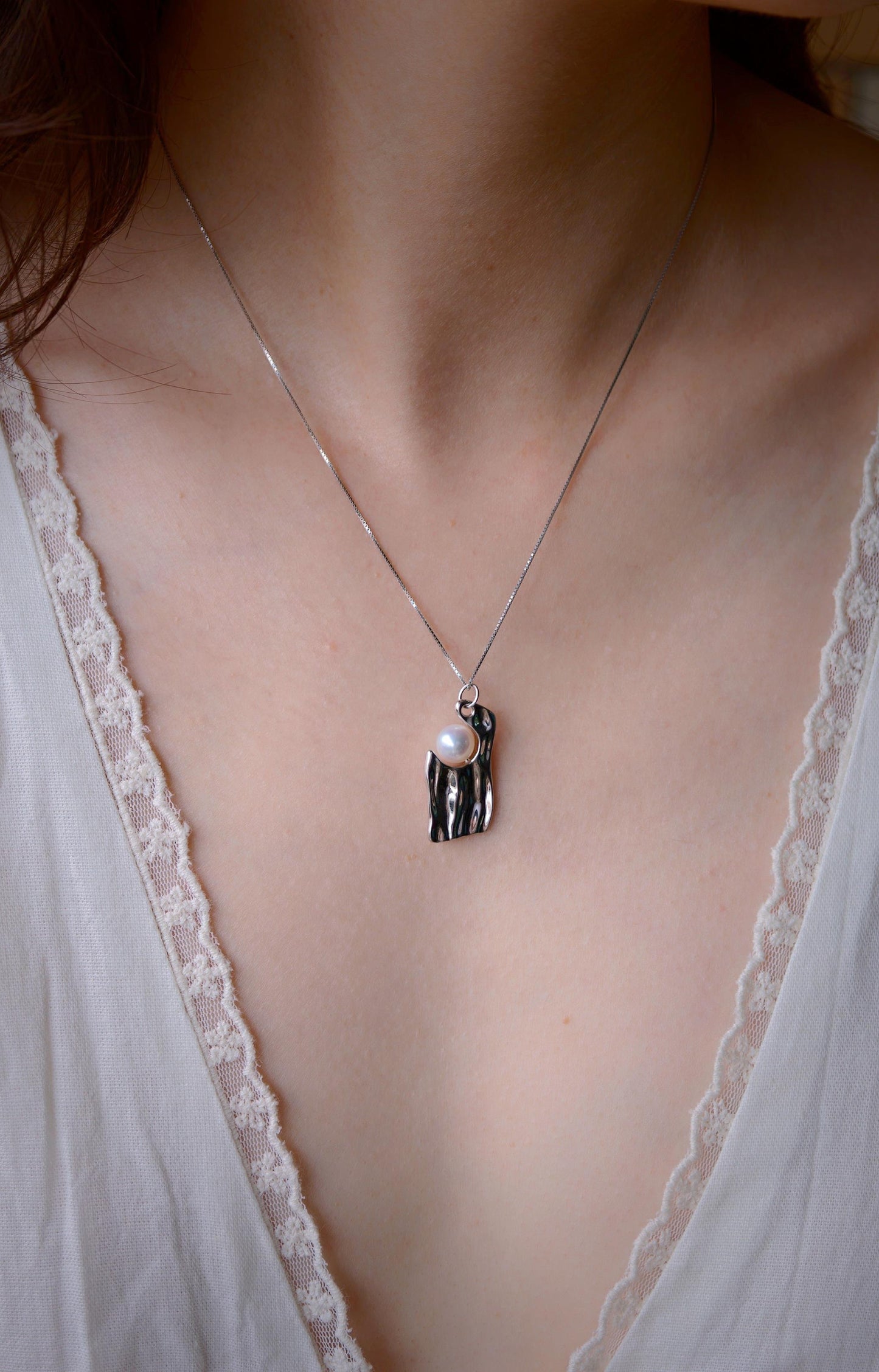 Close-up of Cyrene by Elsie's Ripple Pearl Necklace worn at the neckline, showing the textured silver pendant and round aurora pearl