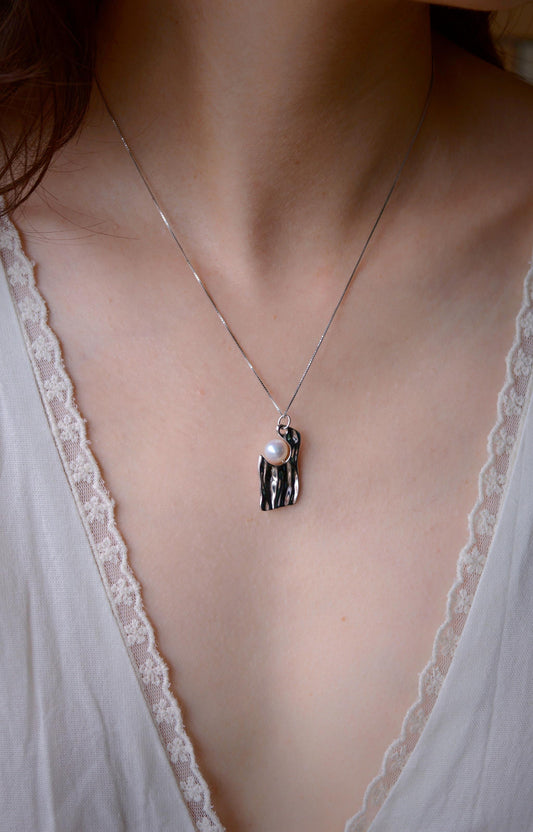 Close-up of Cyrene by Elsie's Ripple Pearl Necklace worn at the neckline, showing the textured silver pendant and round aurora pearl