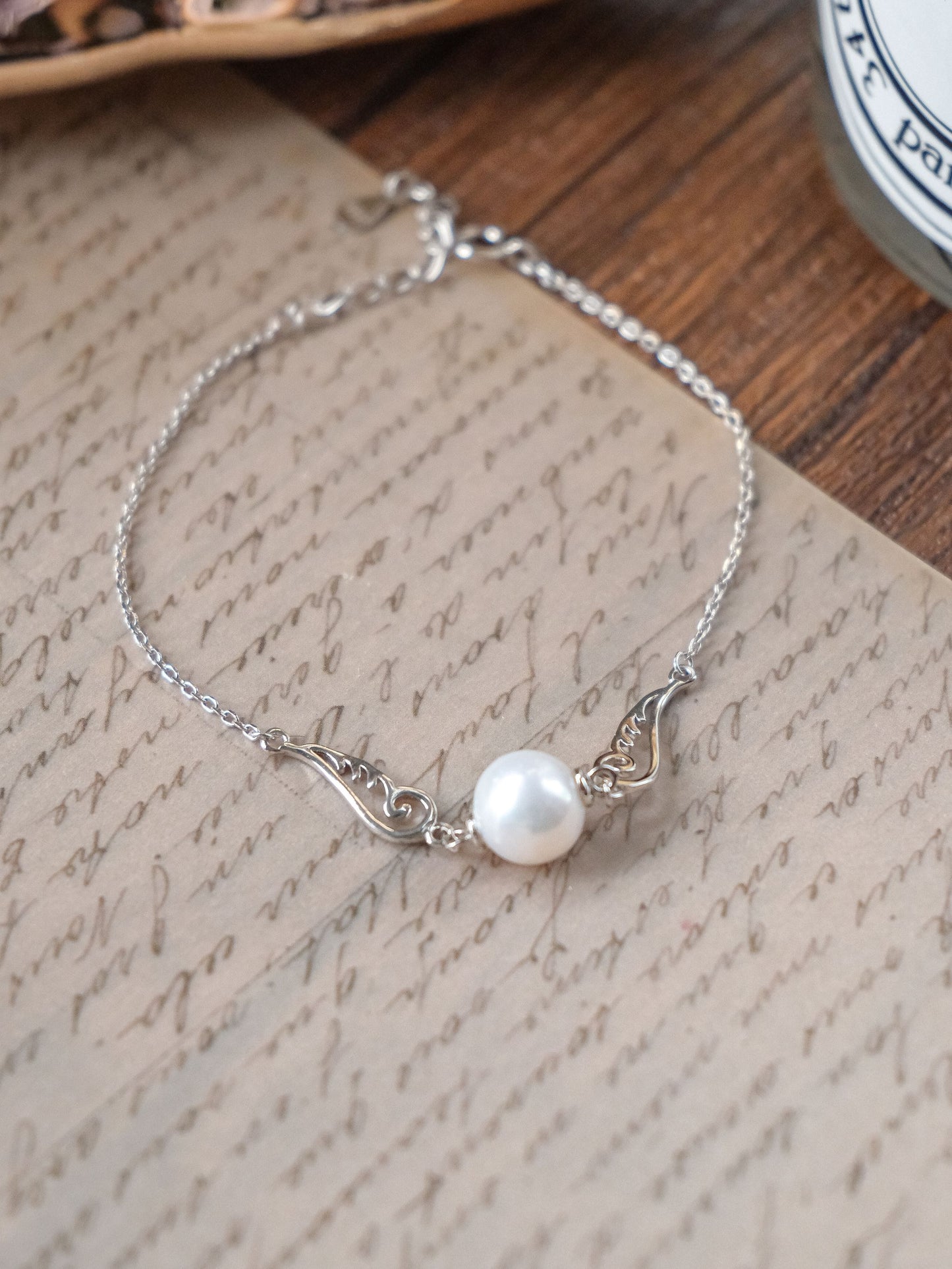 A romantic and sweet silver wing bracelet by Cyrene, showcasing a single pearl on a highly delicate chain.