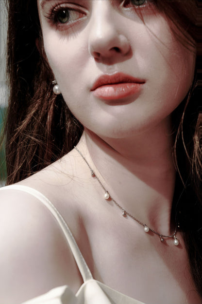 Model wearing Cyrene's romantic teardrop pearl and silver bead necklace, adding a touch of intellectual chic to a delicate white top
