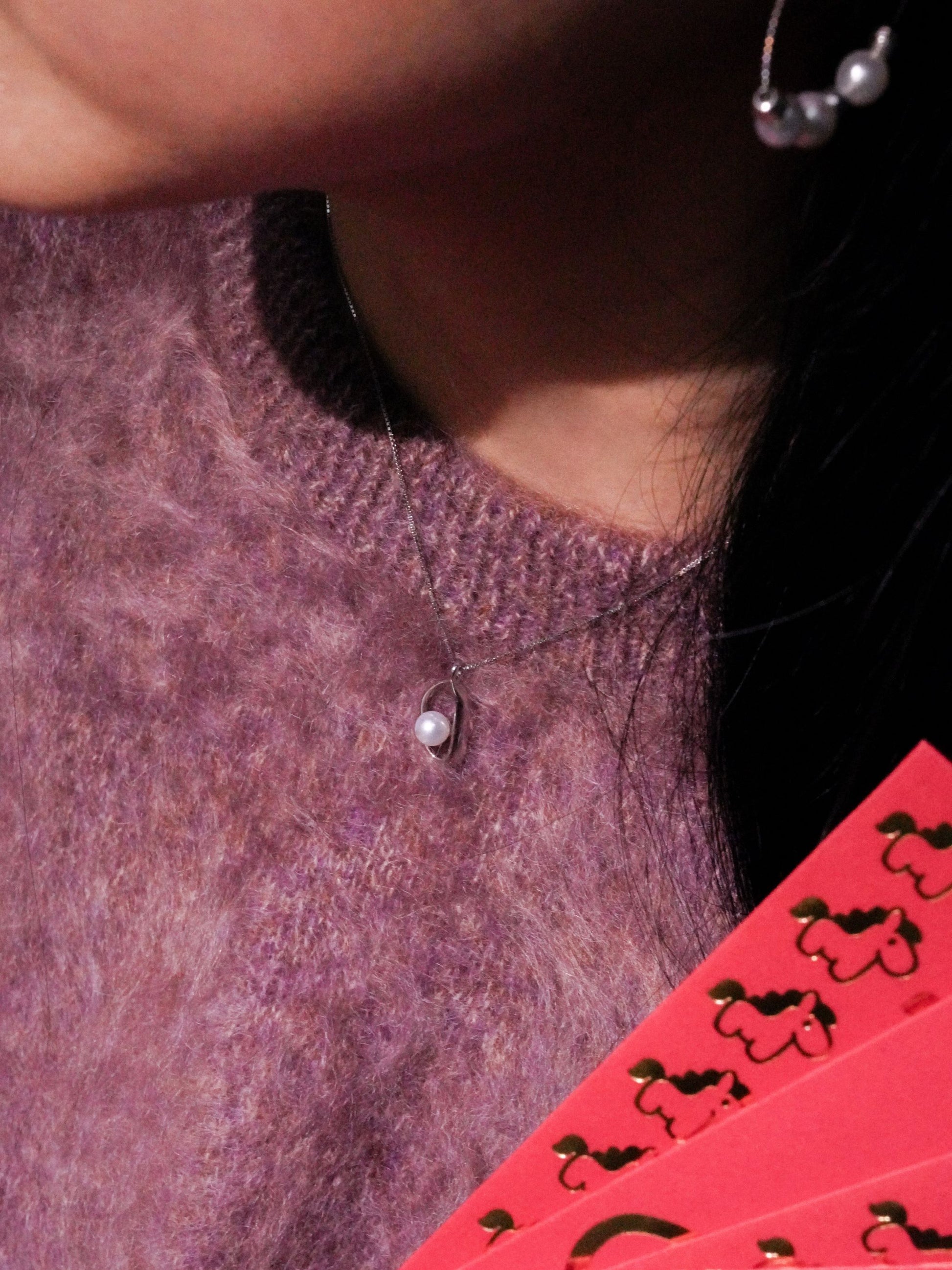 Model wearing a simple and understated Cyrene pearl pendant, styled as a subtle everyday jewelry accent with a cozy sweater.