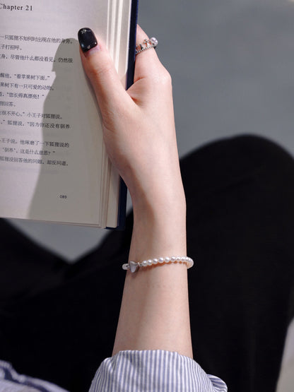 Lifestyle shot of a woman holding a book, elegantly accessorized with Cyrene's delicate seed pearl bracelet with a heart clasp.