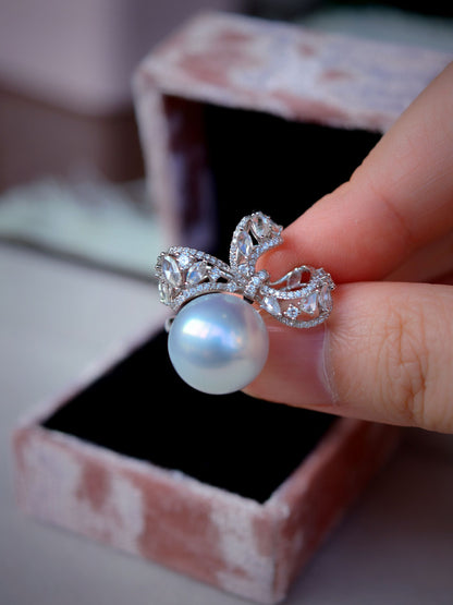Cyrene Solitaire Bow Pearl Ring held between fingers above gift box — South Sea pearl and diamond ring