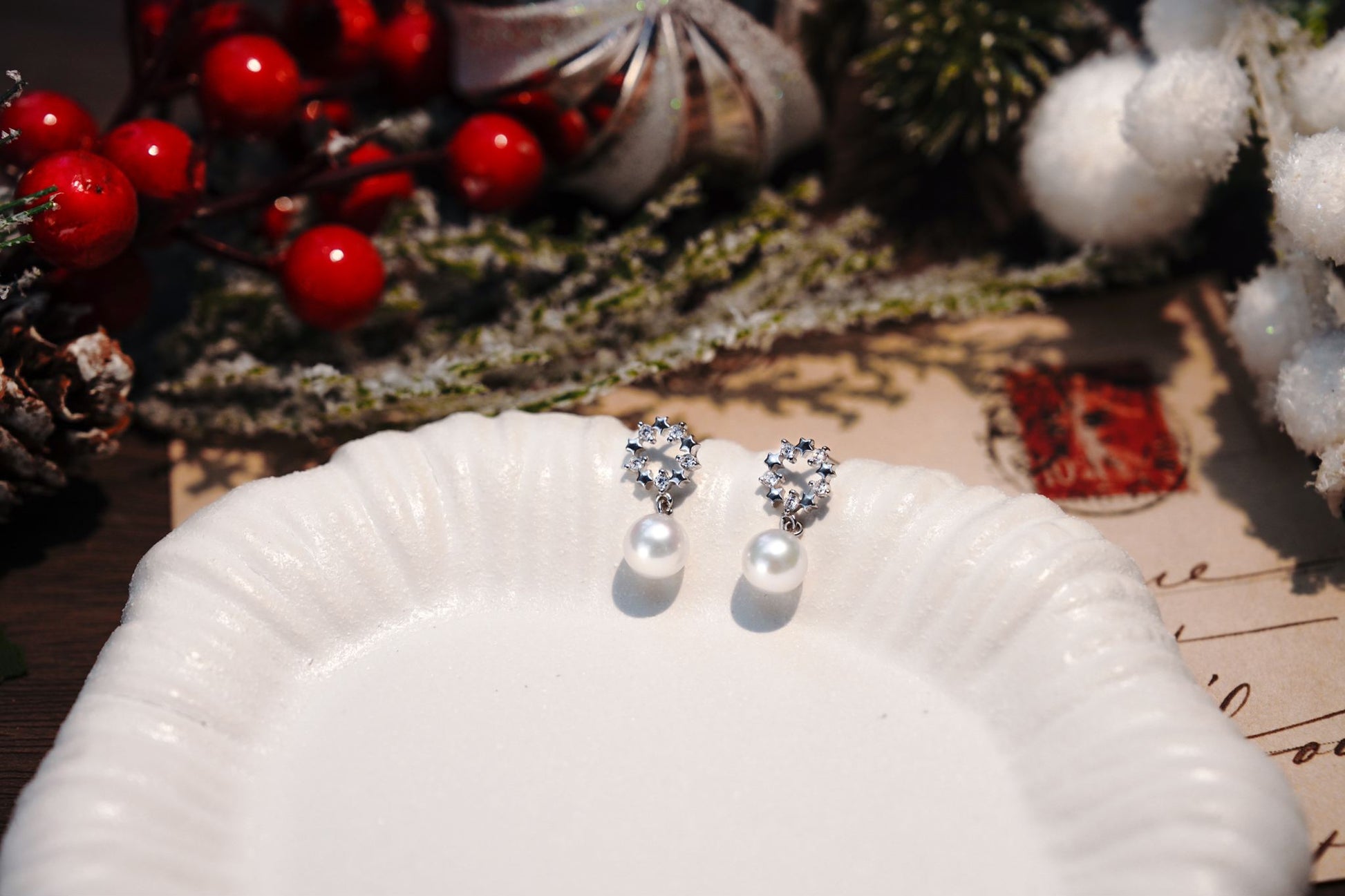 Cyrene's sparkling wreath and pearl drop earrings resting on a white shell plate, a perfect elegant jewelry gift