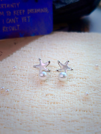 Cyrene Starshore Pearl Earrings — mother-of-pearl starfish studs with round freshwater pearl drops on cream textile, flatlay detail