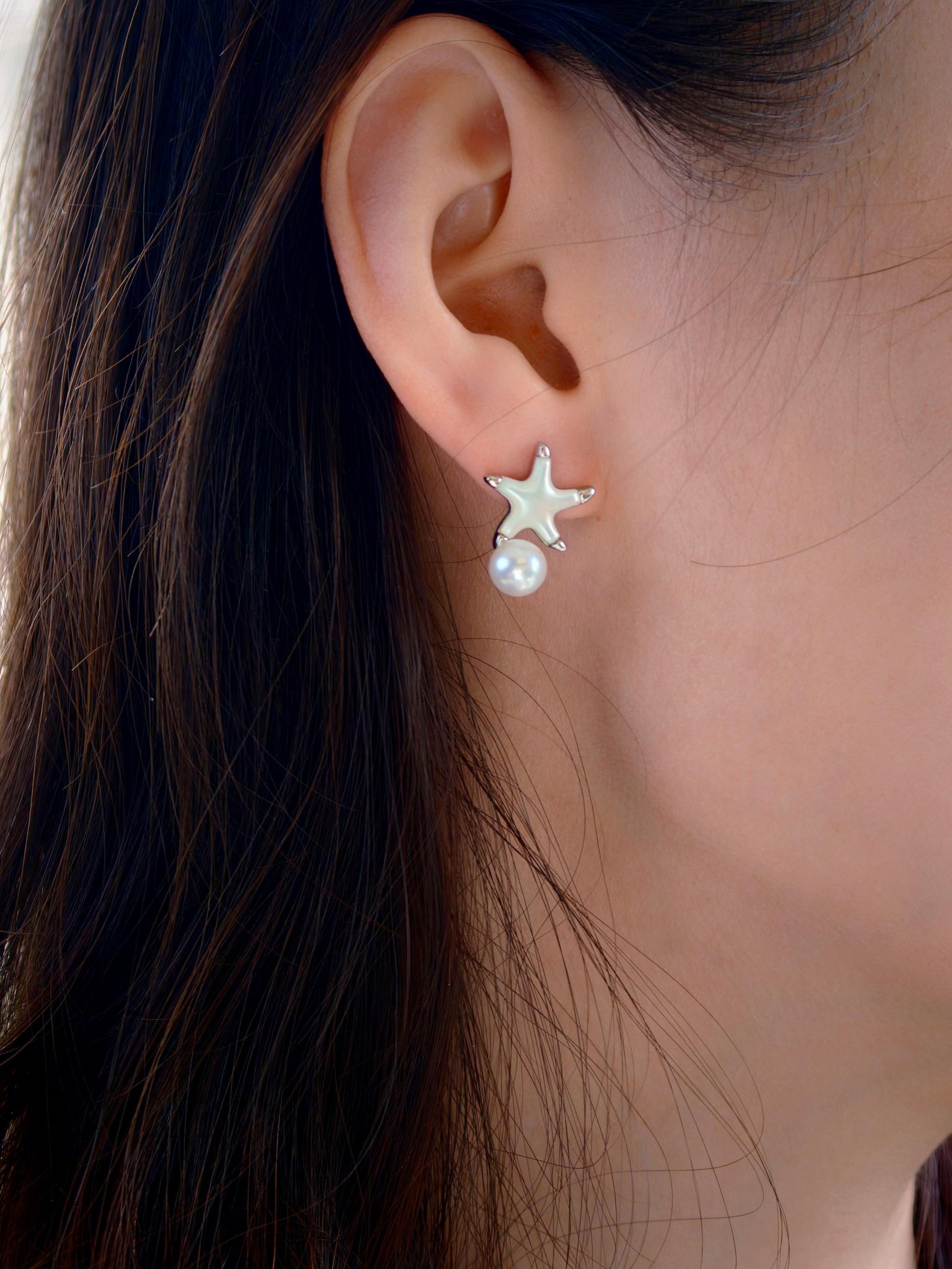 Cyrene Starshore Pearl Earrings worn on ear — sterling silver starfish with mother-of-pearl inlay and 6-7mm round freshwater pearl drop